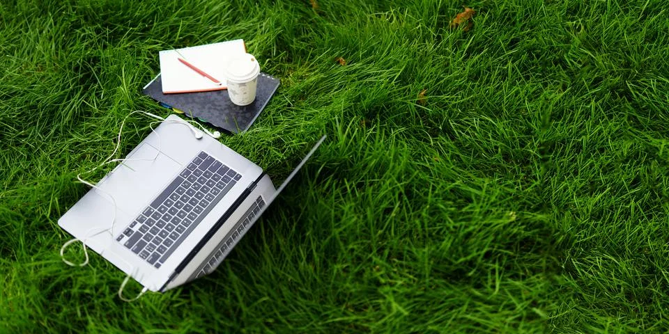 Elements of work or study on the grass, outdoors: an open laptop, a notebook Stock Photos