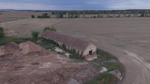 Elevated aerial view of a long weathered agricultural building surrounded by Vídeos de archivo 346034430