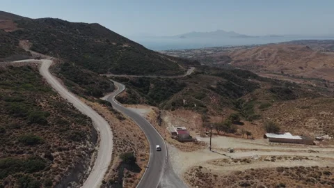 Elevated aerial view of a winding paved road crossing dry rugged hills, with Stock Footage 344142946