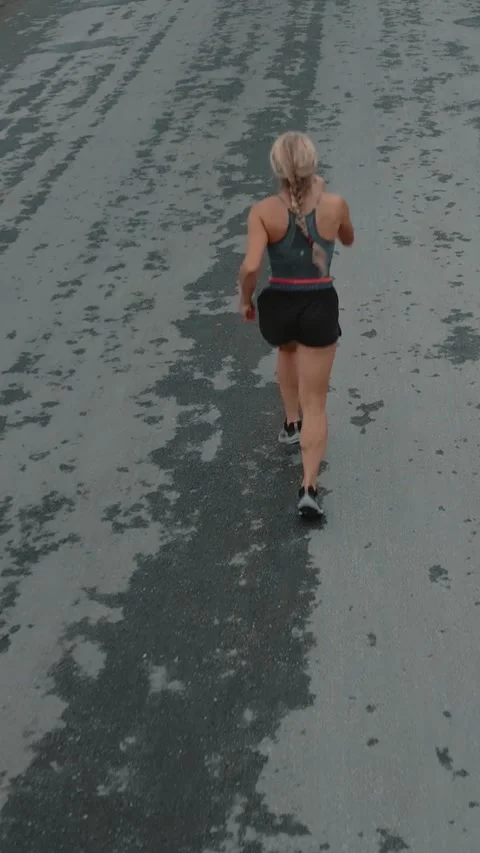 Elevated back view of braided female runner on a textured road Stock Footage 340047017