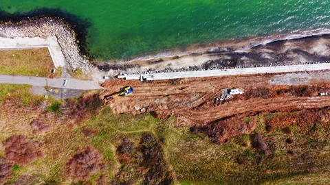 Elevated drone view of coastal seawall construction site with excavator and sea, Stock Footage 337202186