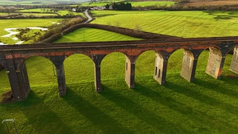 Elevated railway viaduct arching over green countryside with long shadows Stock Footage 309639233