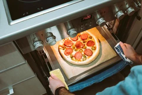 Elevated view of men's hands pulling a finished homemade pizza out of the oven Stock Photos