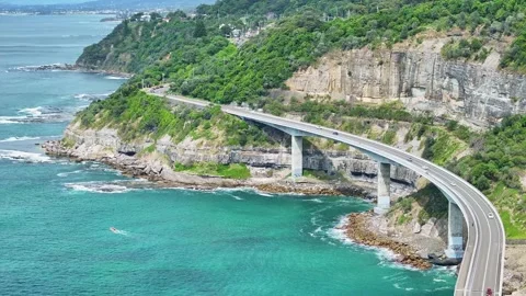 Elevated view of Sea Cliff Bridge hugging the cliffs above the Pacific Ocean Stock Footage 288806022