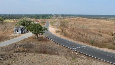 Elevated view of a winding asphalt road through a dry rural landscape with hills Видео 329541695