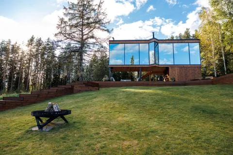 Elevated Wooden House with Angular Design and Fire Pit on Grassy Slope Stock Photos