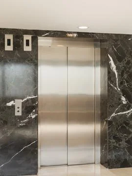 Elevator doors are positioned in a building with dark marble walls. The are.. Stock Photos