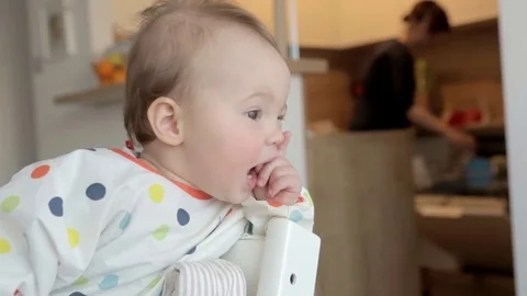 Eleven months old sitting by the table, looking at mother working in the kitchen Stock Footage 73679771