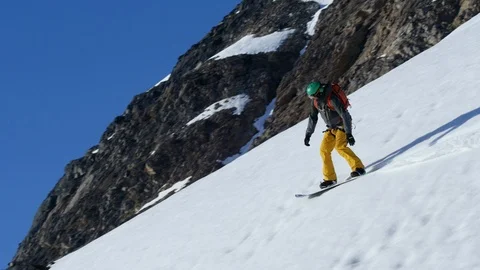 Elite snowboarder speeding down mountain slope towards icy water Stock Footage 113266696