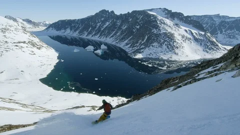 Elite snowboarders speeding down mountain slope towards icy water Stock Footage 113266896