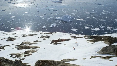 Elite snowboarders speeding down mountain slope towards icy water Stock Footage 113269095