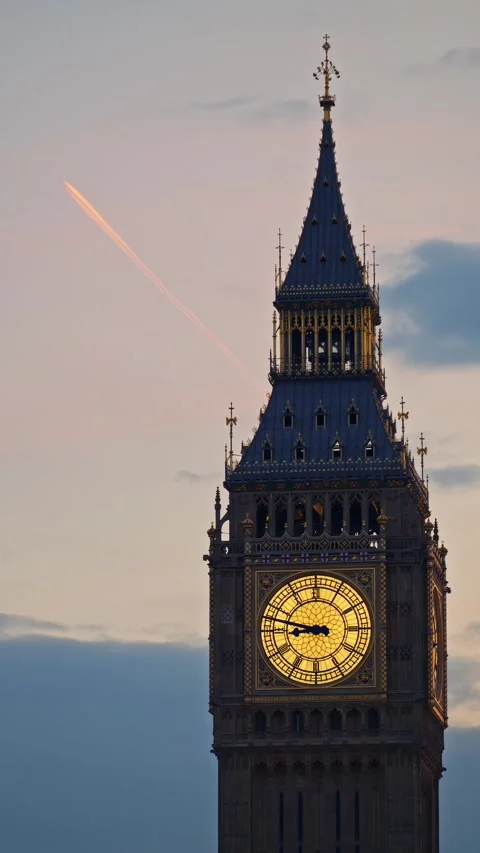 Elizabeth tower big ben clock face illuminated at dusk with contrail streak.. Stock Footage 339460610