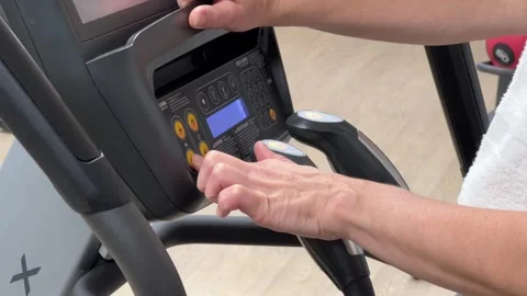 An elliptical cross-trainer is programmed for cardio training by a woman's hand Stock Footage 267609681