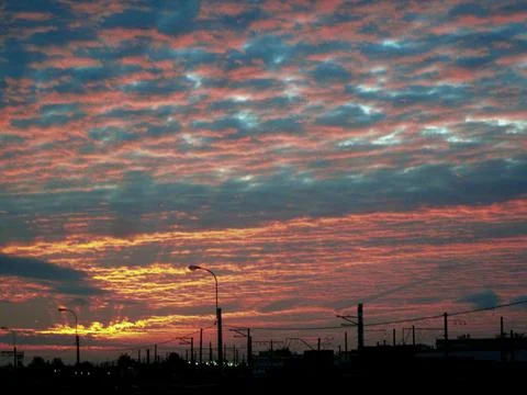 Ellow-orange-blue cloudy sunset over the dark silhouettes of large industrial Stock Photos
