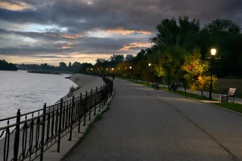 The embankment of a full-flowing river with a pedestrian road with lanterns a Stock Photos