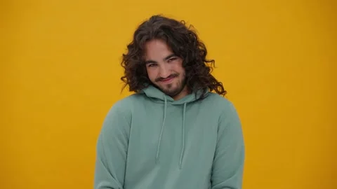 Embarrassed long-haired man looking at camera in yellow studio Stock Footage 231902974
