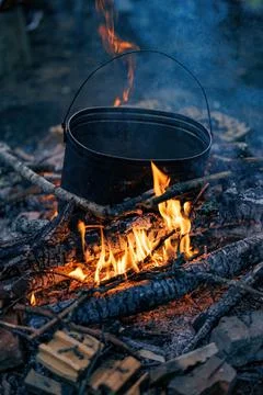 Embers Dance Beneath a Cauldron: A timeless pot simmers over a roaring camp.. Foto stock