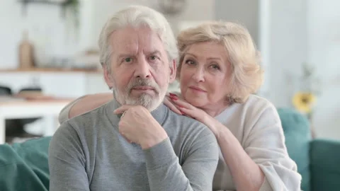 Embracing Senior Old Couple Looking at Camera while Sitting on Sofa Video stock 148200734