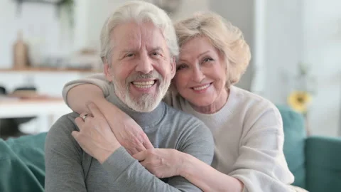 Embracing Senior Old Couple Smiling at Camera while Sitting on Sofa Video stock 148202201