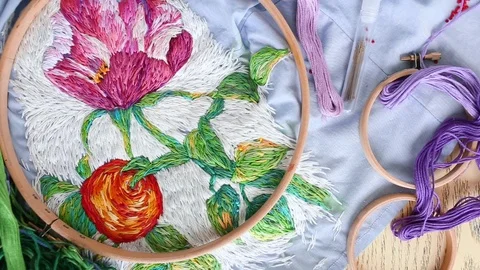 Embroidery hoops, threads, needles on embroidered fabric with colorful pattern Stock Footage 118319987