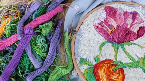 Embroidery hoops, threads, needles on embroidered fabric with colorful pattern Stock Footage 119921536
