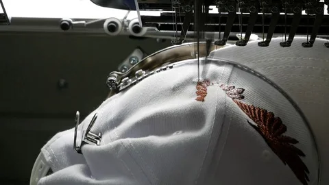 The embroidery machine creates an emblem on the cap's surface Stock Footage 90395361