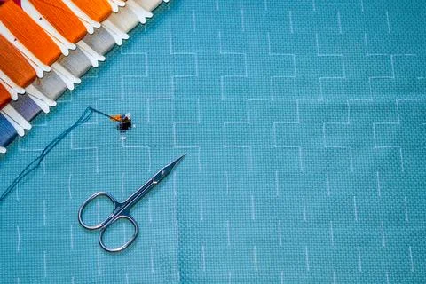 Embroidery scissors and threaded needle on blue cross stitch fabric with Stock Photos