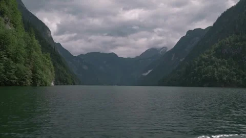 Emerald Alpine Lake Reflecting Forested Mountains and Moody Cloudy Sky Stock Footage 315071248