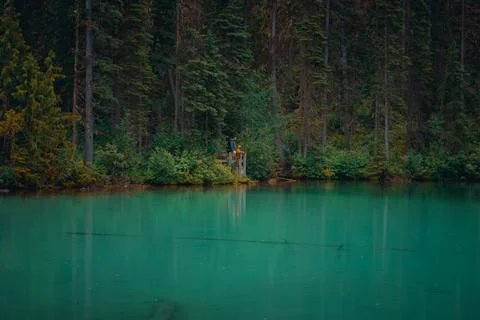 Emerald lake with figures at a viewing platform surrounded by a green forest Stock Photos