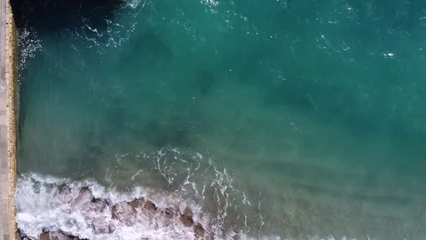 Emerald wave washes a beach sea with concrete pier and large boulders, top view Stock Footage 126646175