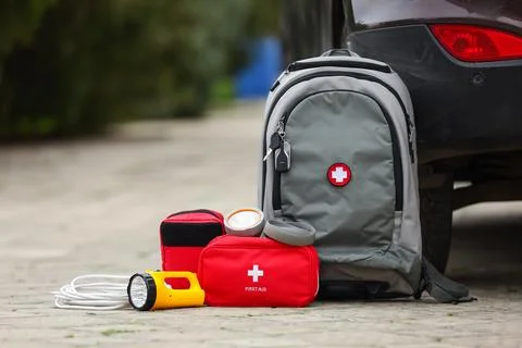 Emergency backpack, first aid kit and necessities near car outdoors Stock Photos