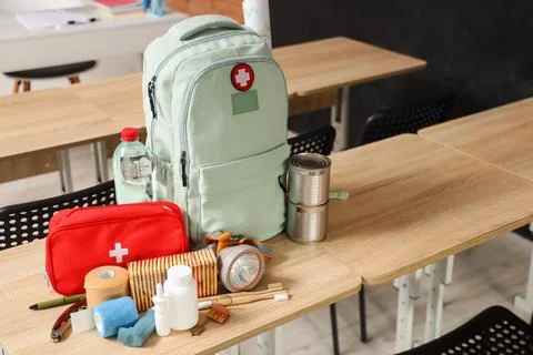 Emergency backpack, first aid kit and necessities on table in empty classroom Stock Photos