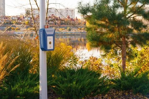 Emergency call box, panic alarm in autumn park by lake with pine tree and c.. Stock Photos