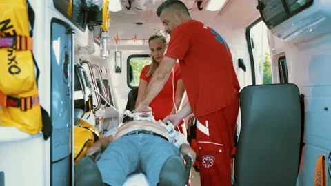 Emergency team using defibrillator shocking old male patient in ambulance car Stock Footage 211820105