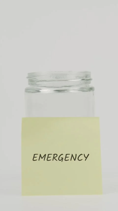 Emergency text or word on yellow sticky note attached to glass jar with hand Stock Footage 311725276