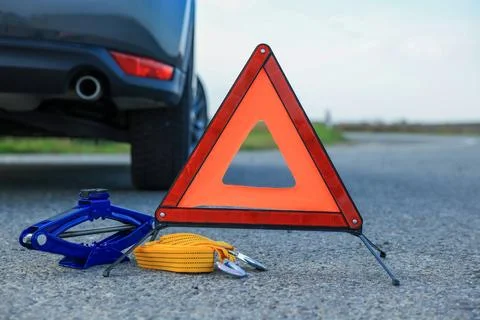 Emergency warning triangle, towing strap and scissor jack near car outdoors.. Stock Photos