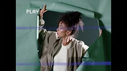 Emerging female model pushing through torn green paper in studio, wearing bomber Stock Footage 332804643