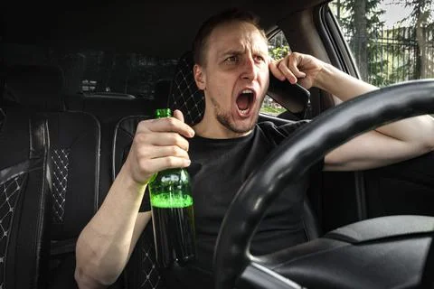 Emotianal Drunk aggressive driver with a bottle of beer driving a car swears on Stock Photos