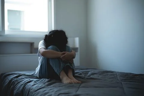 Emotional isolation and deep reflection of a person sitting on a bed in a d.. Stock Photos