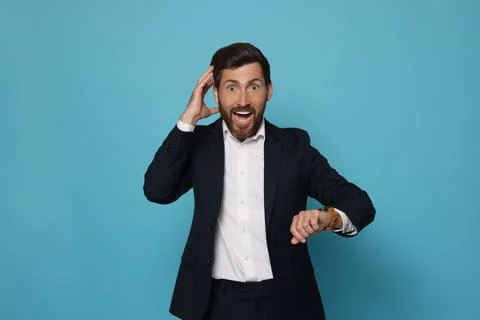 Emotional man checking time on light blue background. Being late concept Stock Photos