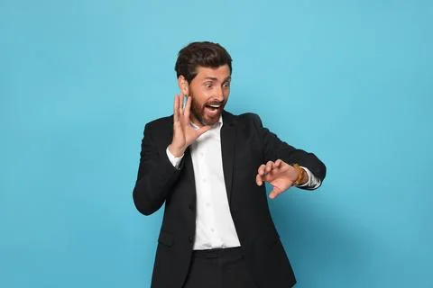 Emotional man checking time on light blue background. Being late concept Stock Photos