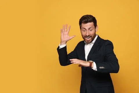 Emotional man checking time on orange background, space for text. Being lat.. Stock Photos