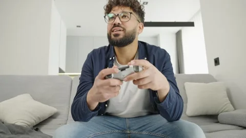 Emotional man with controller playing video game on sofa at home Video stock 333981957