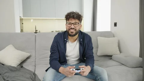 Emotional man with controller playing video game on sofa at home Stock Footage 333981965