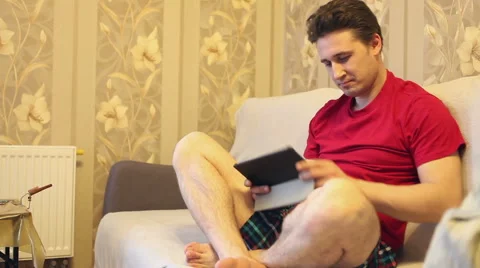Emotional man playing on a tablet while sitting on a sofa Stock Footage 60423105