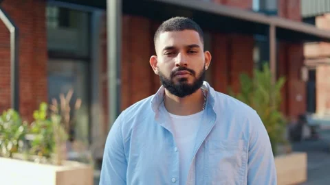 Emotionless man standing still and posing at camera on blurred city background Video stock 250072889