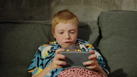 Emotions of a child while playing on the phone on the sofa in his room Stock Footage 233574681