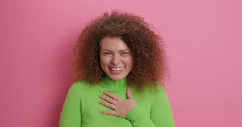 Emotions concept. Overjoyd curly haired woman laughs out joyfully dressed in Stock Footage 154773520