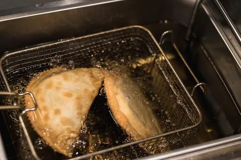 Empanadas are being deep-fried in a metal basket submerged in bubbling oil, s Stock Photos
