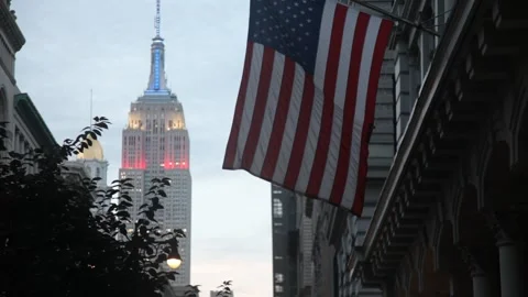 Empire State Building lit at dusk behind an American flag Vidéo 341019128